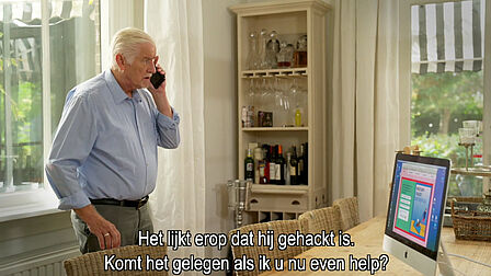 Een man telefoneert over zijn computer. De helpdesk lijkt een fraudeur.